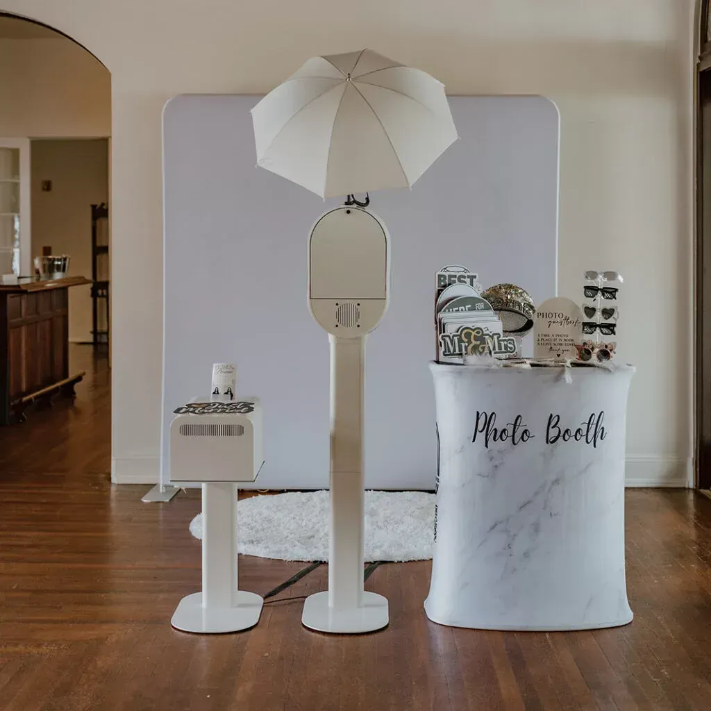 Photo booth setup with a white backdrop, machine, accessories, and a marble-patterned table.