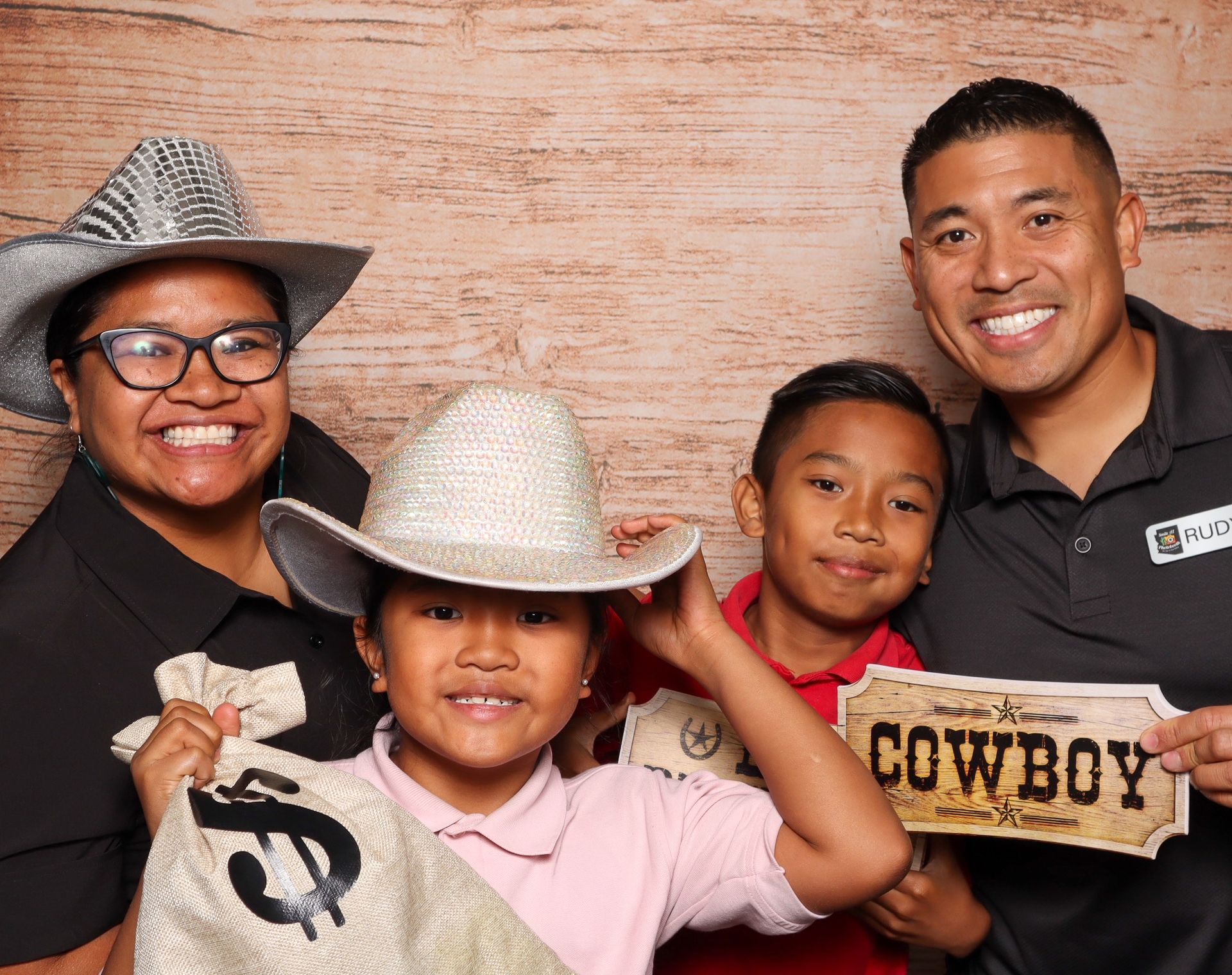 Two people smiling, posing in a photo booth. The person on the right has an arm around the other, holding a skeletal hand.