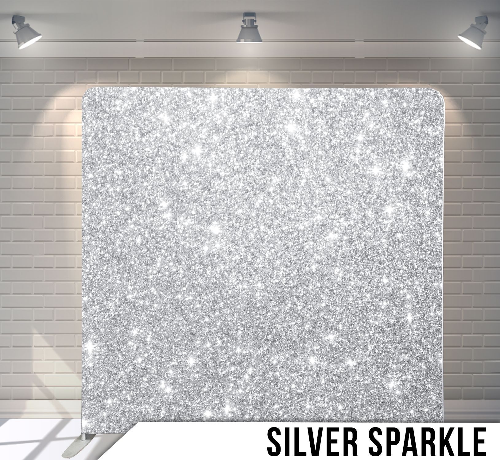 Silver glitter backdrop on a white stand, lit by spotlights, set against a brick wall.