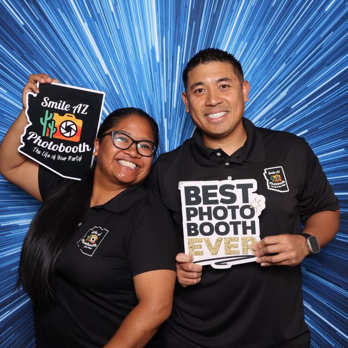 Two people holding photo booth signs against a blue background, smiling.