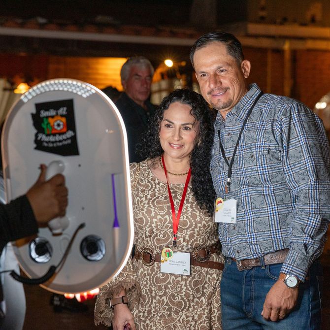 Couple posing for a photo with a photo booth at an outdoor event.