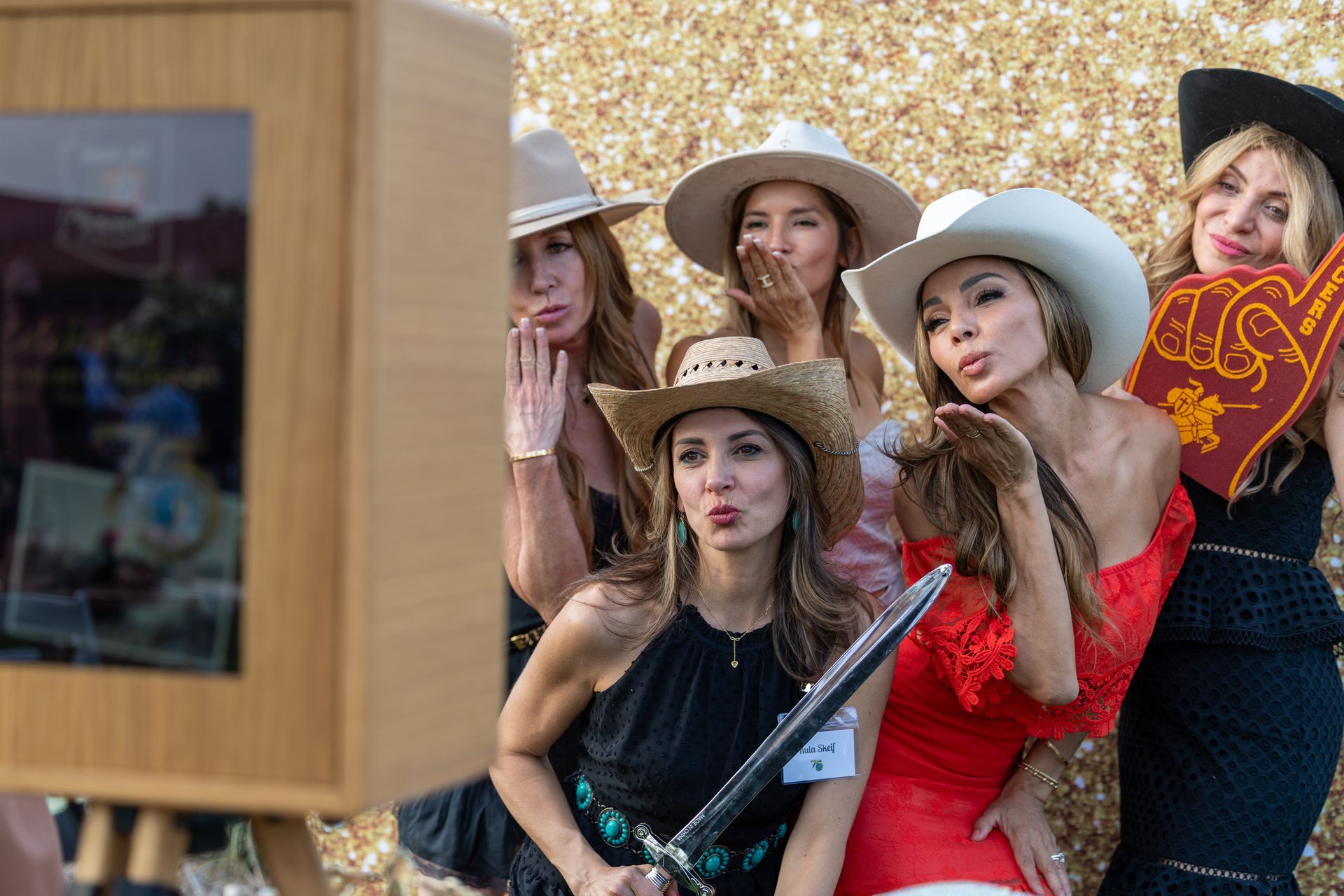 Four people in a photo booth, wearing silly hats and glasses, holding a 