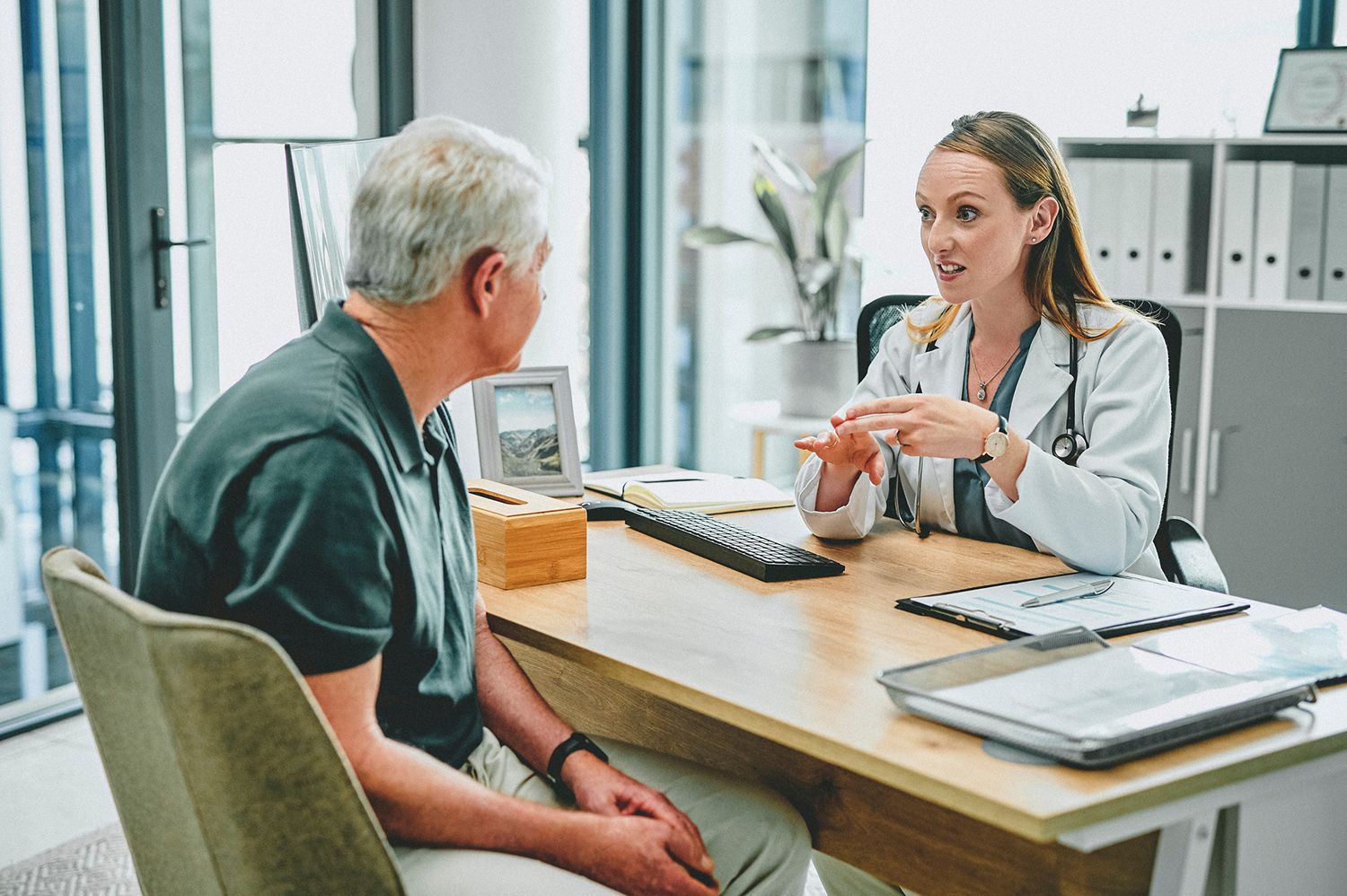 A doctor is talking to an older man who is sitting at a desk.