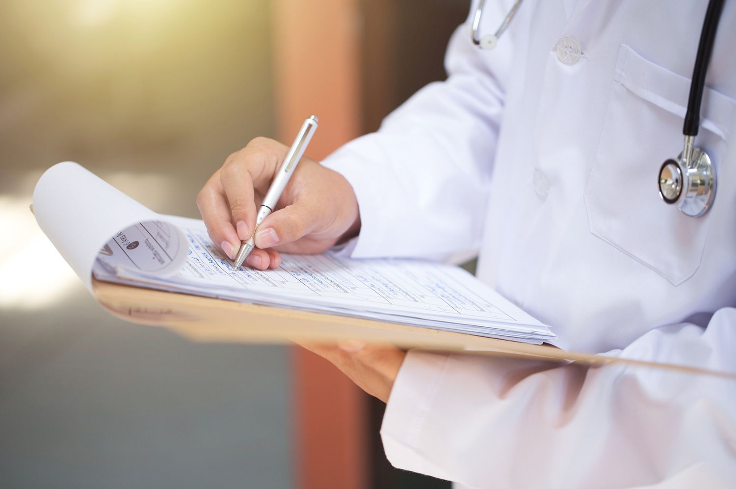 A doctor is writing on a clipboard with a pen.