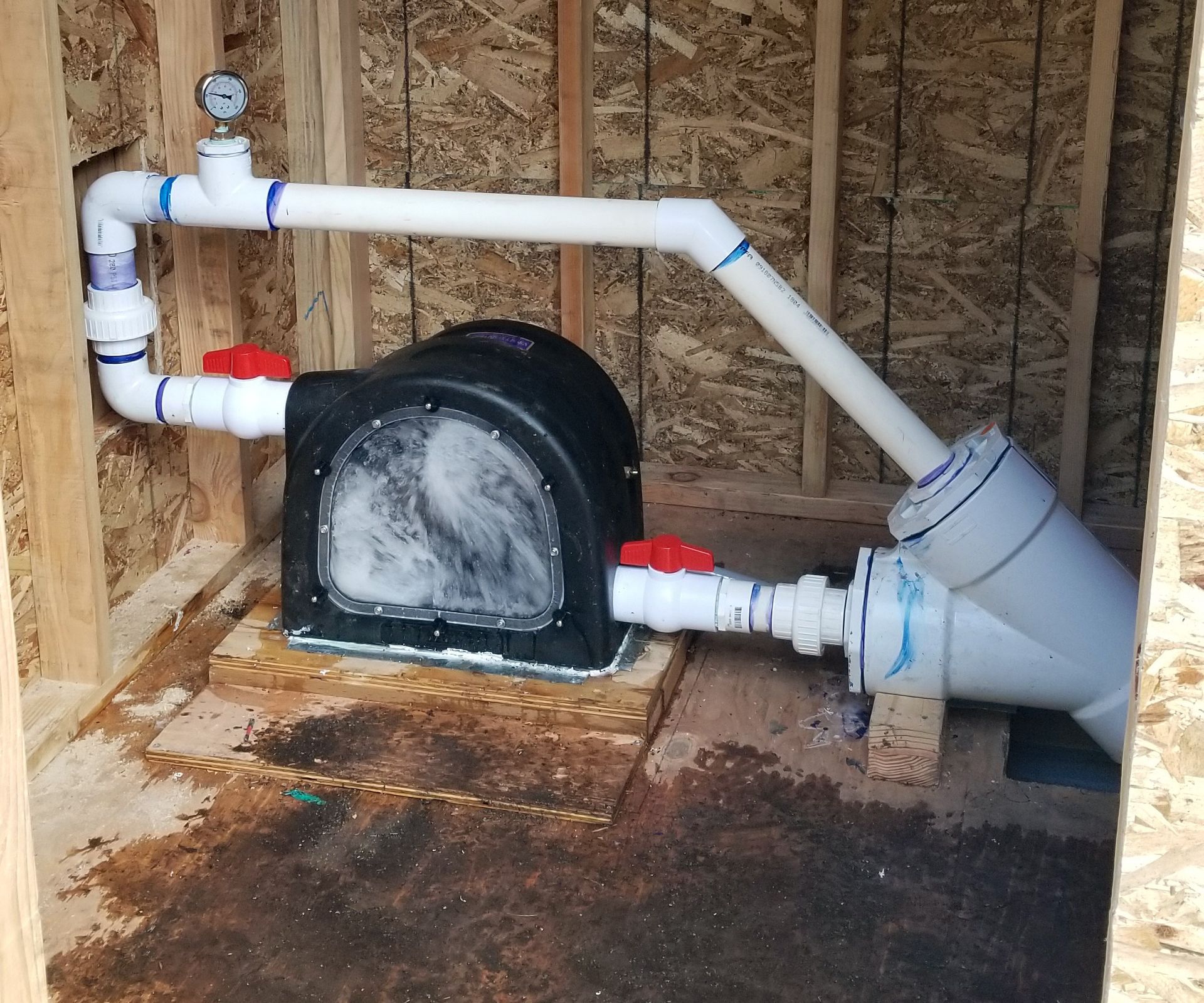 Water pump system with PVC pipes and valves in a wooden enclosure.