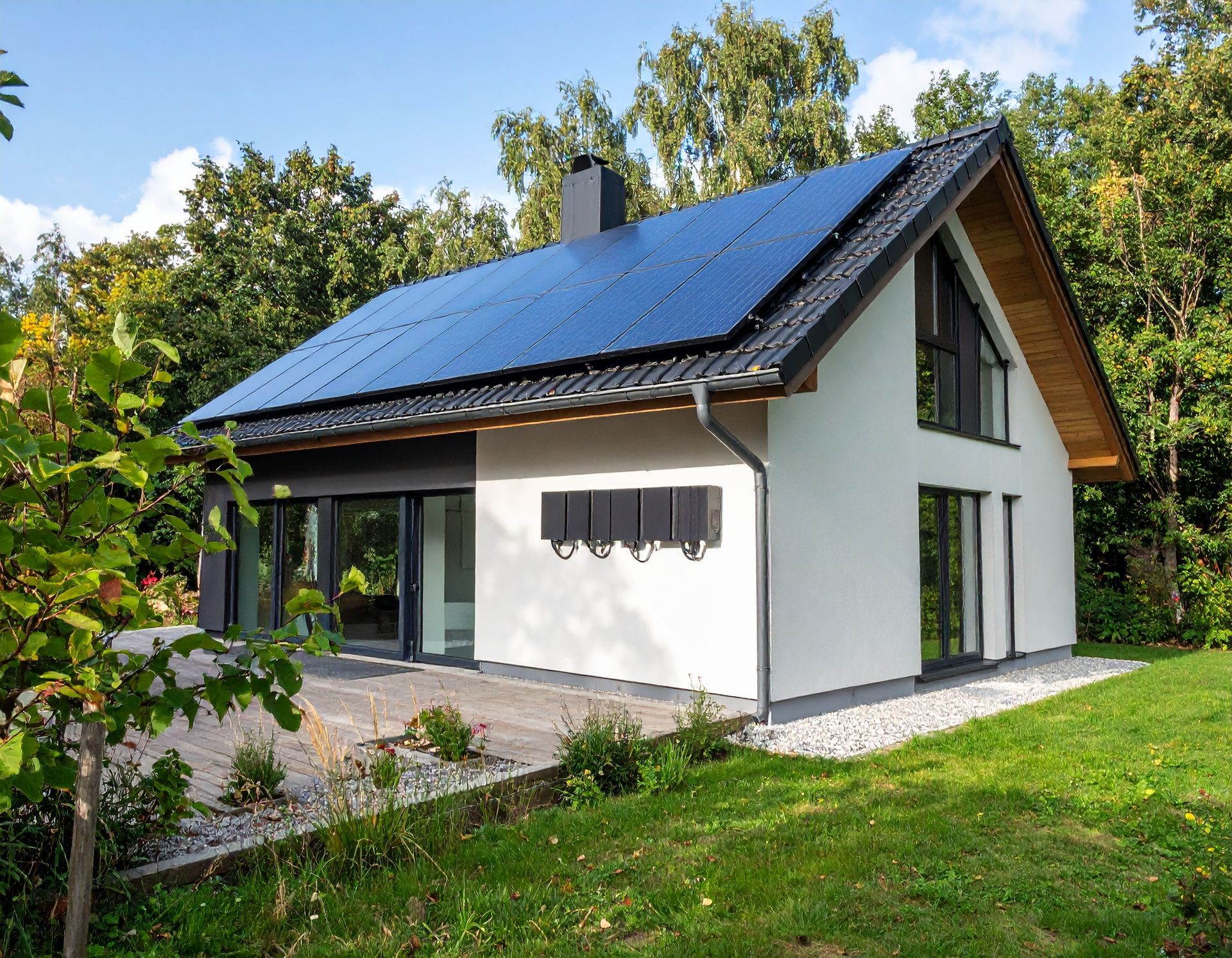 Modern two-story house with a solar panel roof, white exterior walls, and large windows, surrounded by trees and grass.