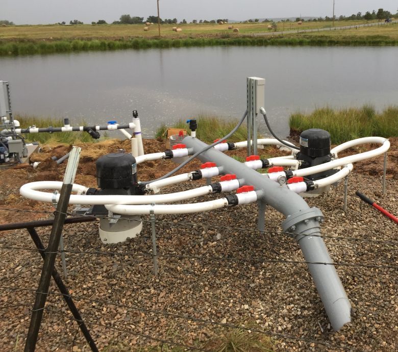 Water pump system with pipes and valves near a body of water.