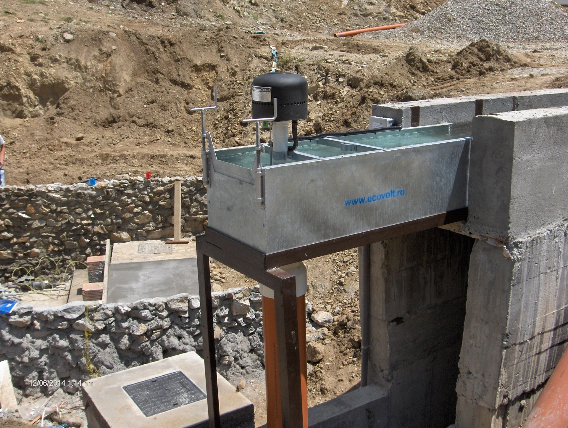 Galvanized metal water flow measuring device mounted on concrete in an outdoor construction site.