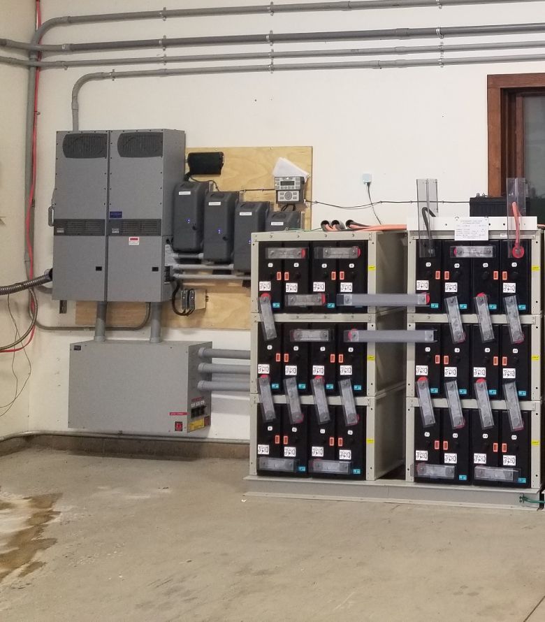 Electrical equipment, including battery array, mounted on a wall in a room. Gray and black components.