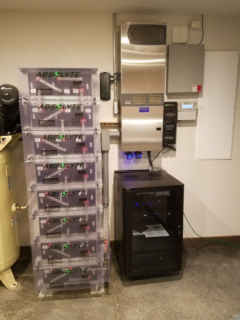 Solar power system components: battery stack, inverter, control panel, mounted on a garage wall.