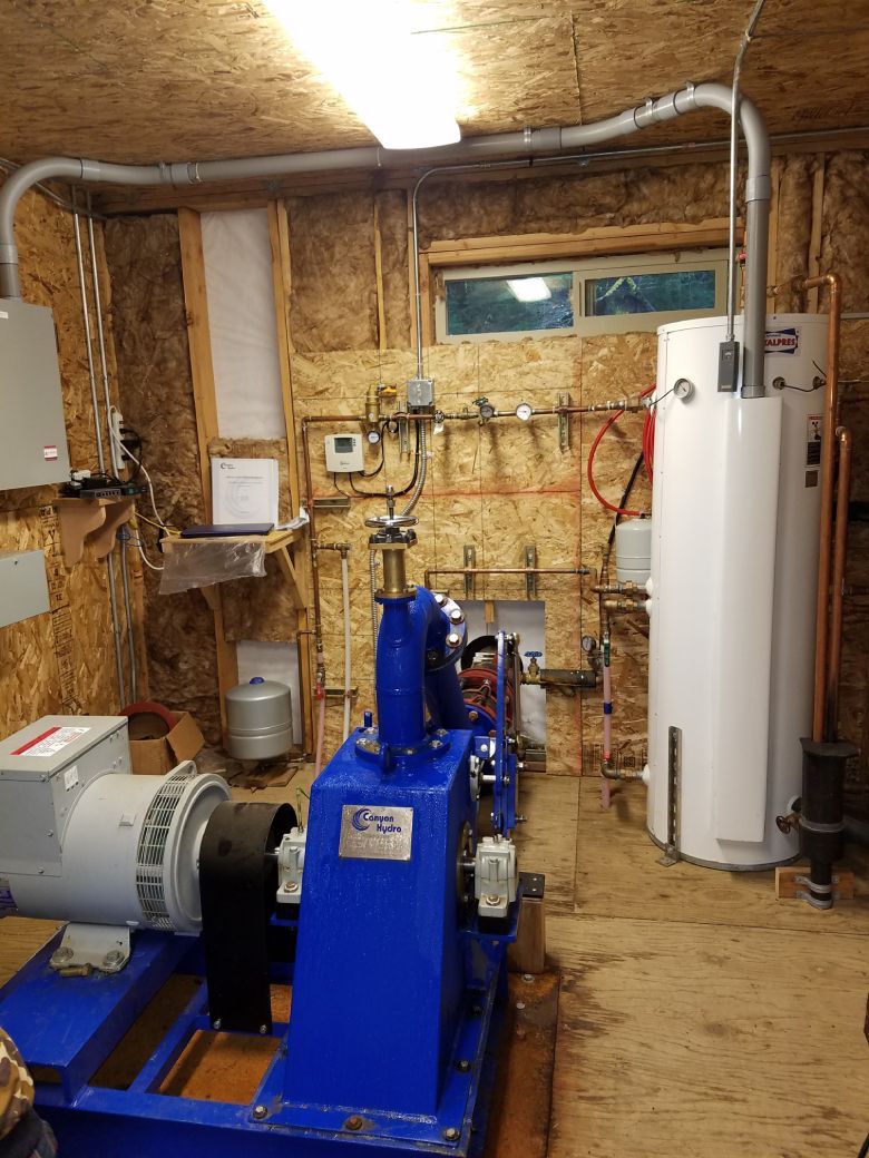 Interior of a utility room with generator, water heater, and electrical components against wood panel walls.