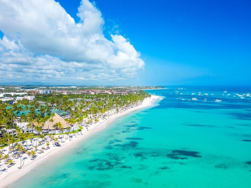 Aerial view of a white sand beach with turquoise water and blue sky, dotted with boats.