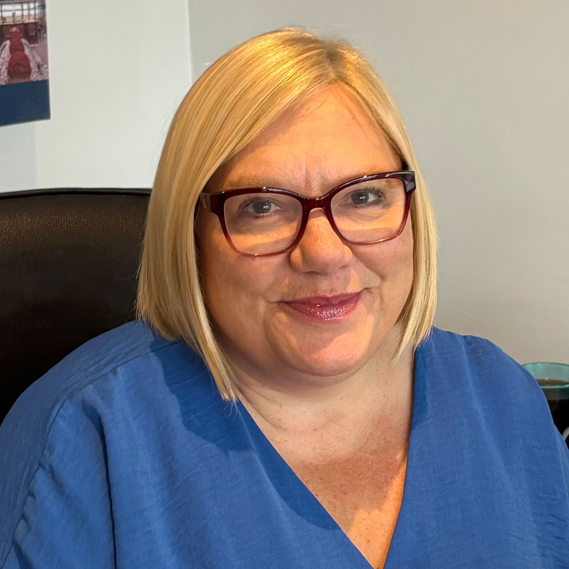 Woman with blonde bob and glasses wearing a blue top, smiling.