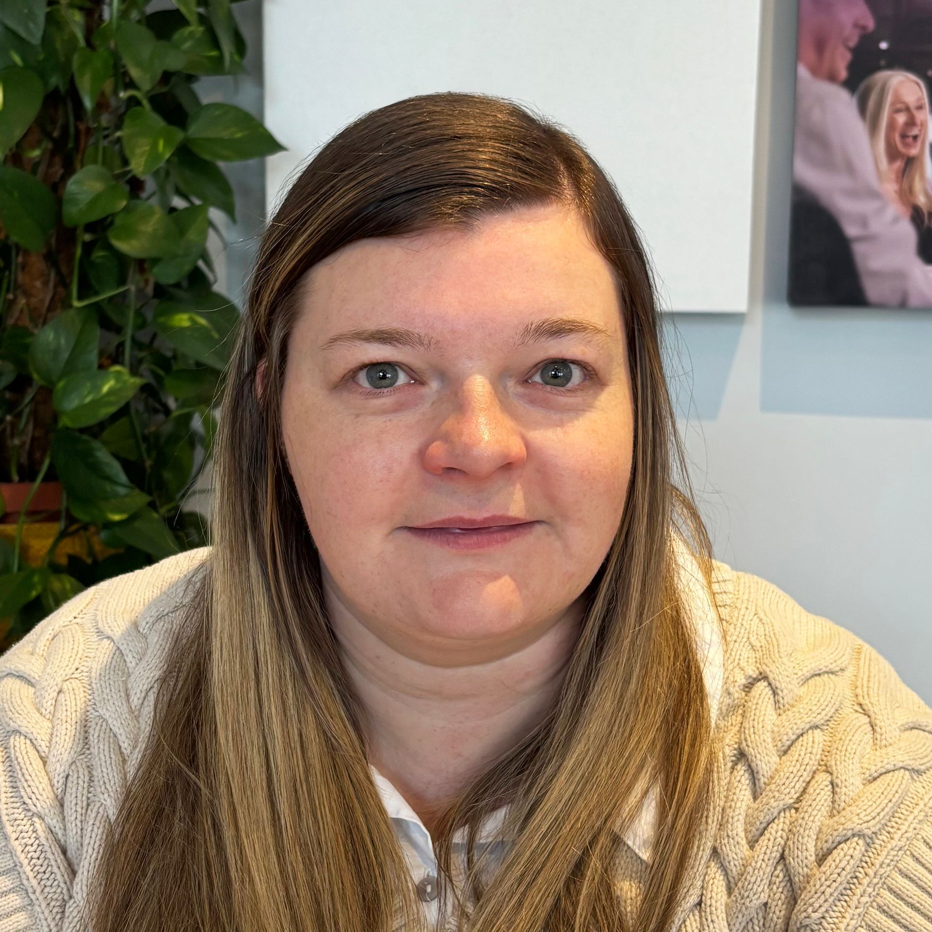 Woman with light brown hair in a white cable-knit sweater, looking at the camera.