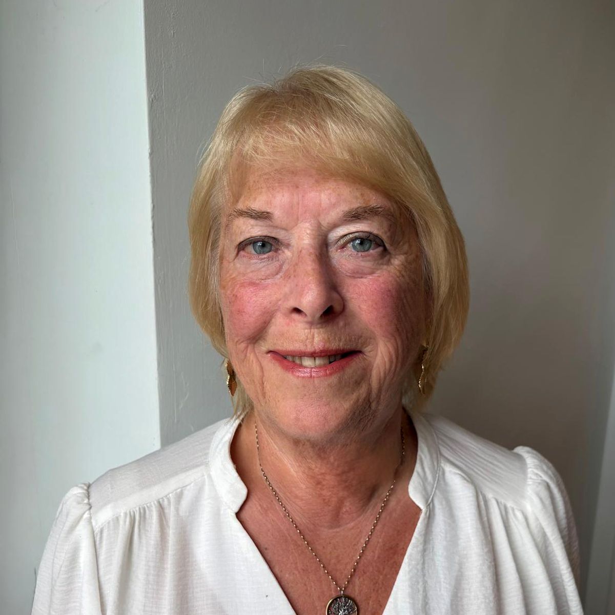 Woman with blonde hair wearing a white top smiling at the camera.