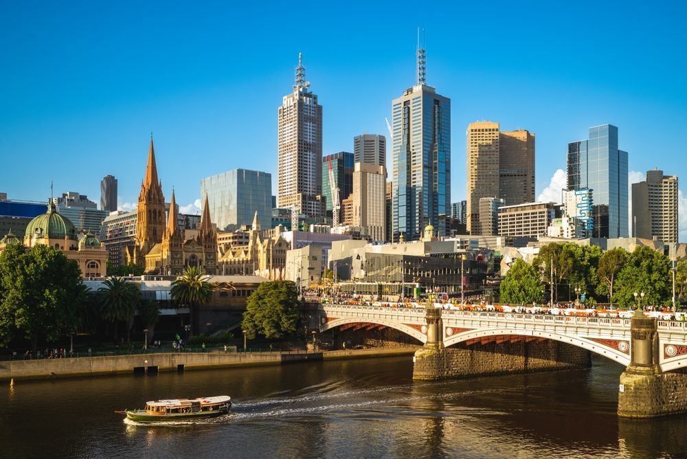 Melbourne city skyline with skyscrapers, a bridge, and a river on a sunny day.