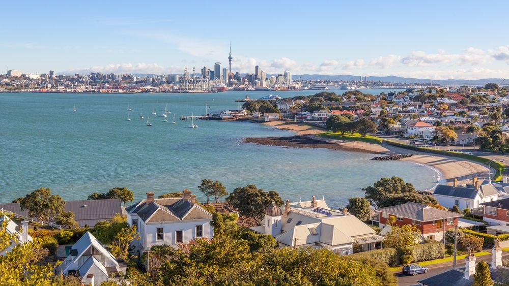 Auckland, New Zealand, coastal view: cityscape with waterfront homes and the Sky Tower in the distance.
