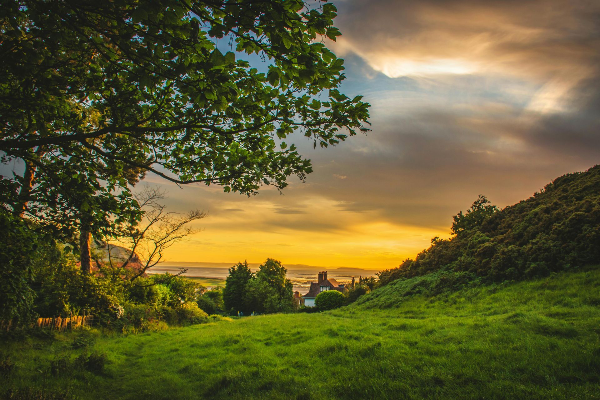 Sunset over a green field with trees, a small town, and dramatic clouds.