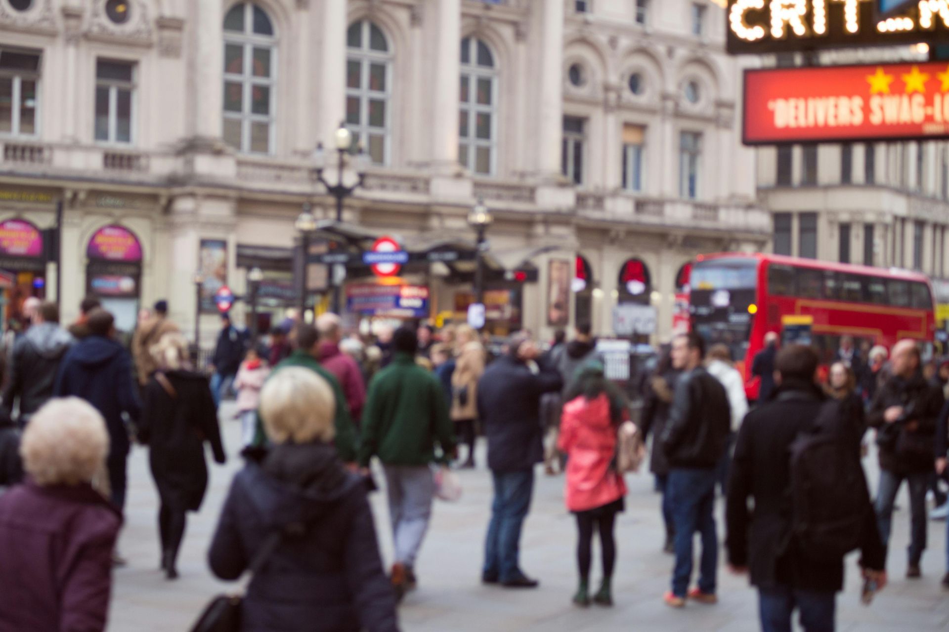 Blurred crowd in Piccadilly Circus, London, near buildings and a red double-decker bus.