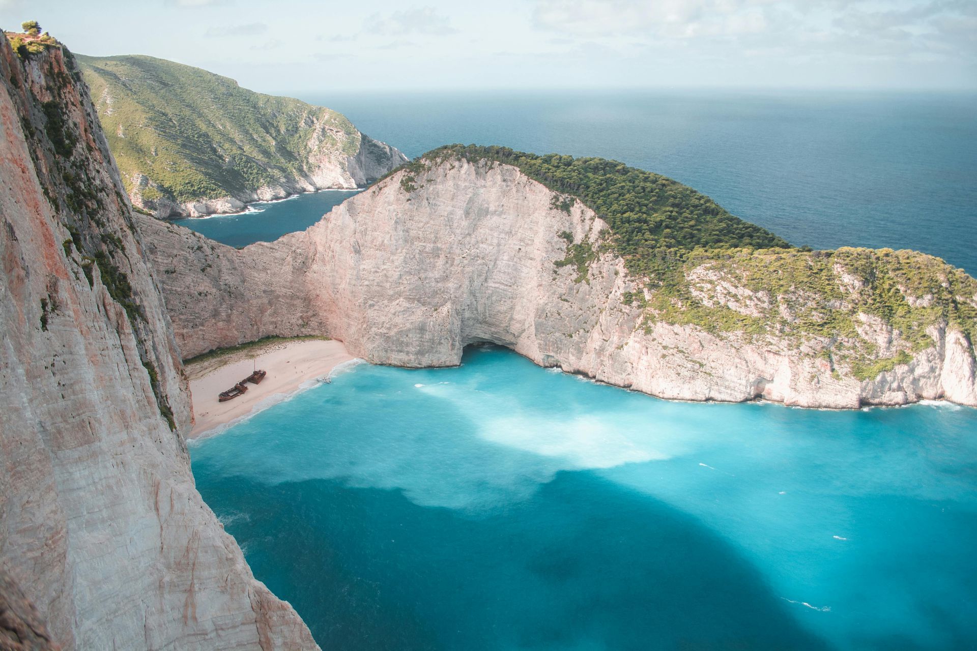 Turquoise water, white cliffs, and green hills surround a beach with a shipwreck; Zakynthos, Greece.