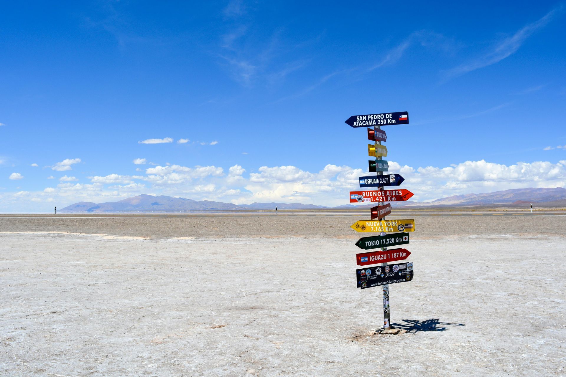 Signpost with multiple colored signs in a desert landscape against a blue sky.