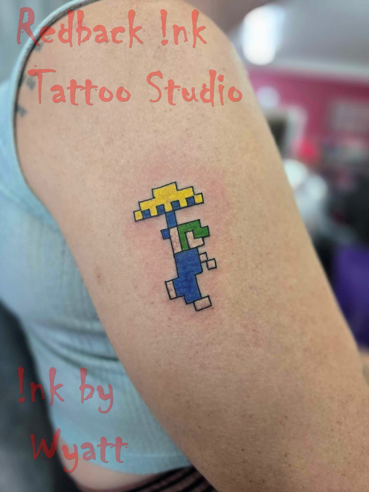 Pixelated Luigi Tattoo on Upper Arm, Holding a Yellow Mushroom, Blue Overall — Redback !nk Tattoo Studio in Kawana, QLD