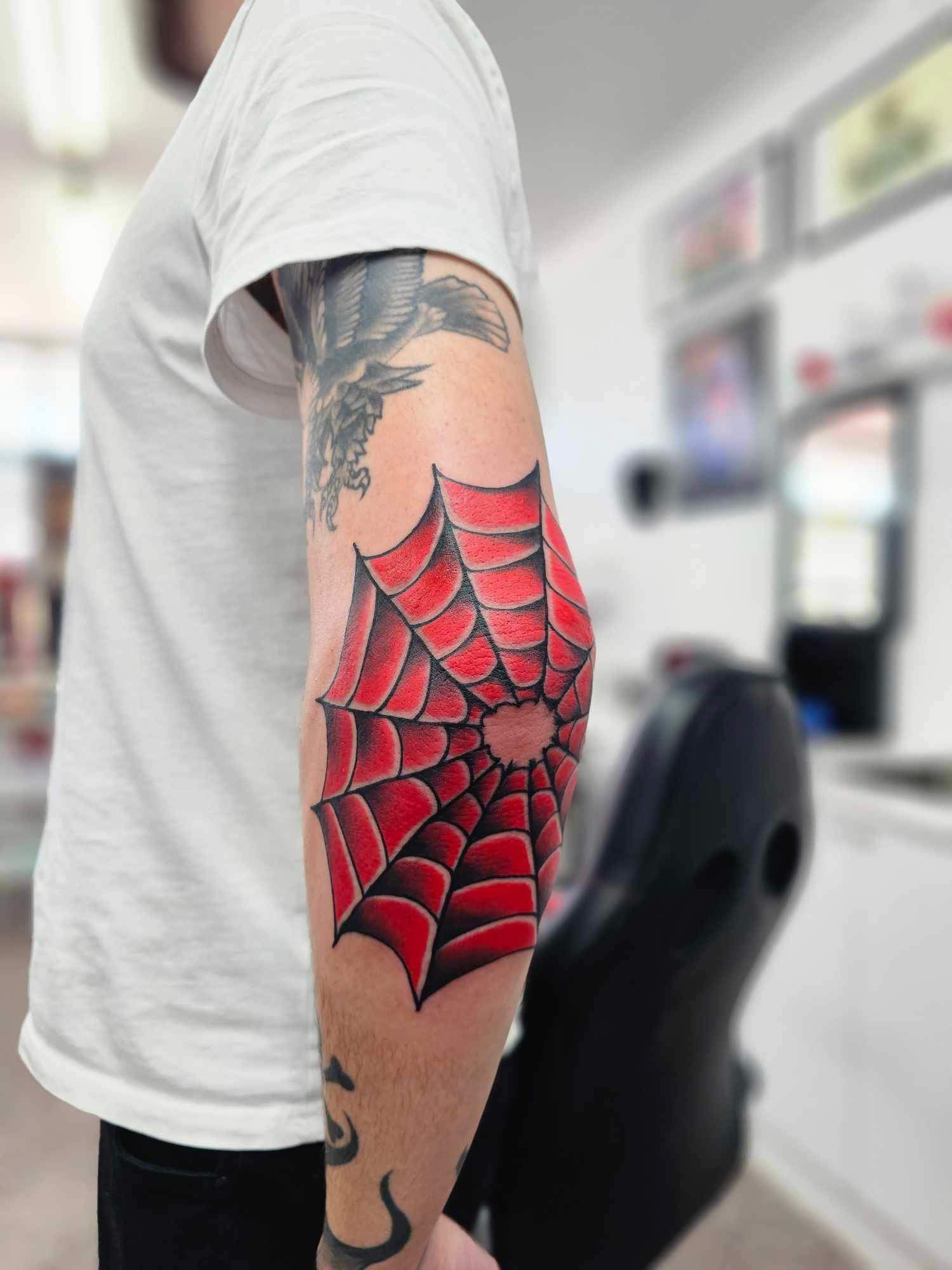 Tattoo of a Red Spider Web on a Person's Elbow. They Are Wearing a White Shirt — Redback !nk Tattoo Studio in Kawana, QLD
