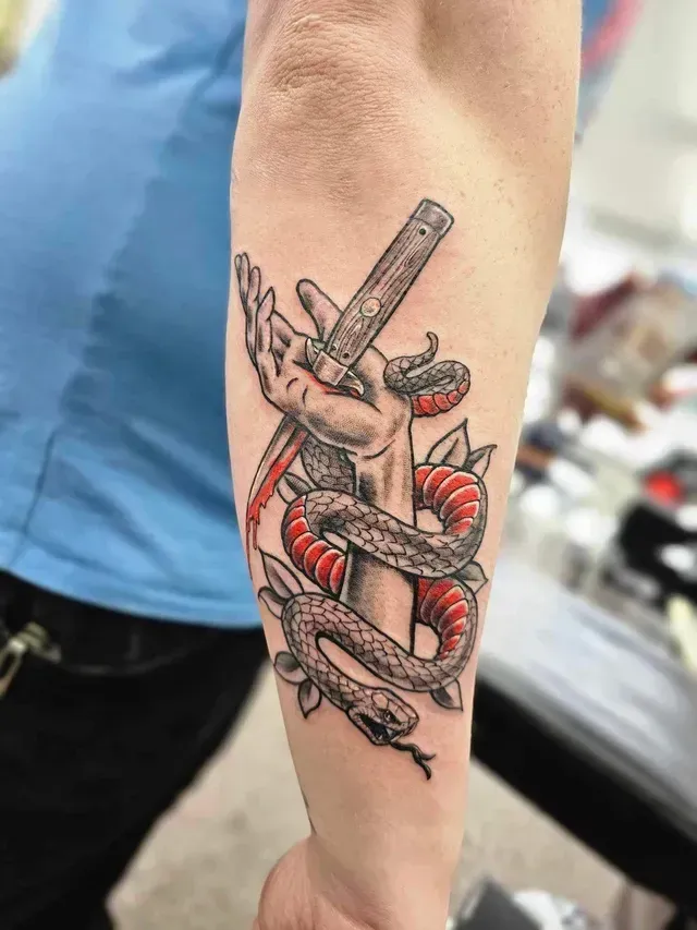 Tattoo of a hand holding a straight razor, wrapped by a red and black snake.