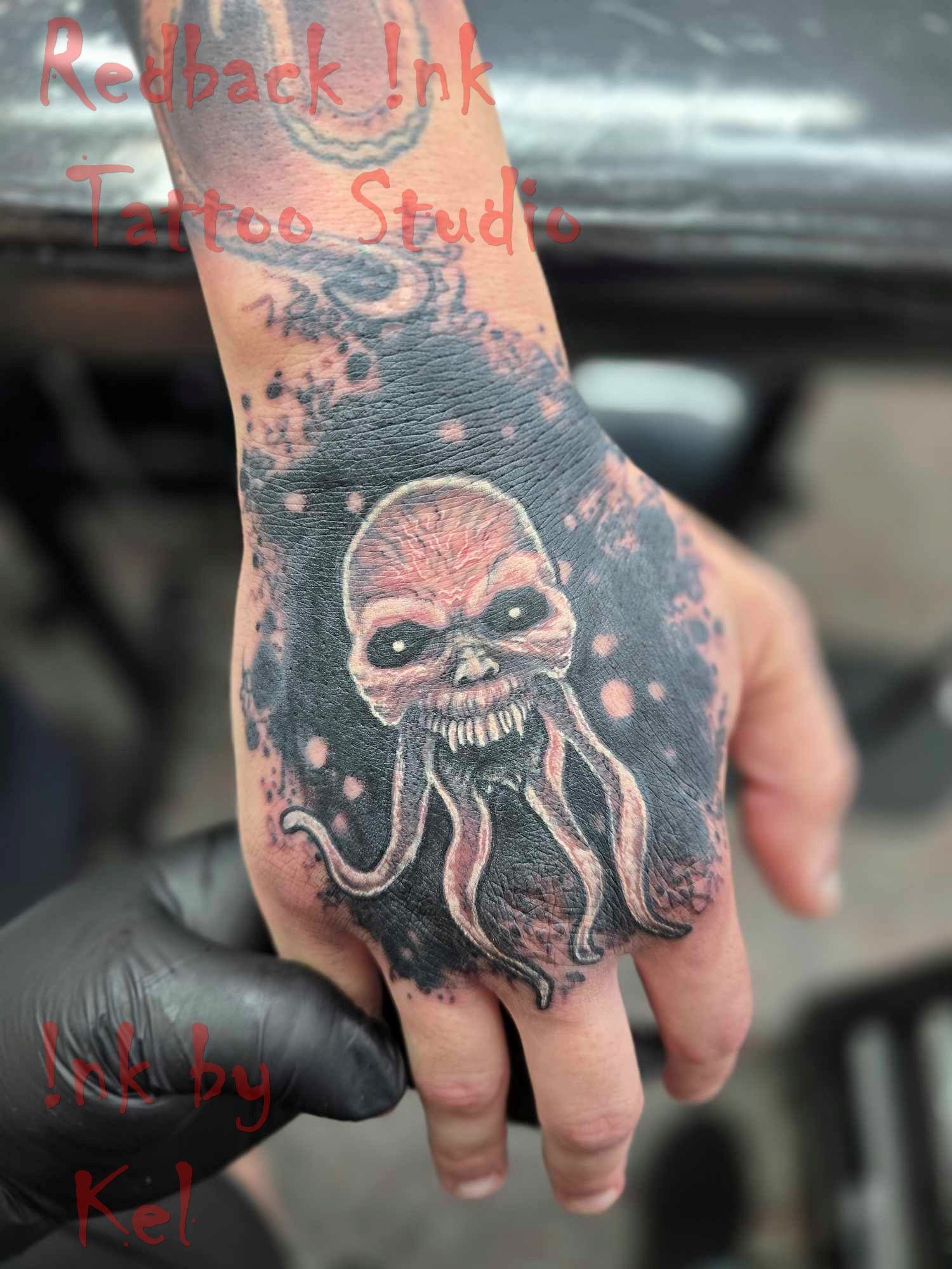Tattoo on hand: a skull-like creature with tentacles, surrounded by black ink, held by a gloved hand. — Redback !nk Tattoo Studio in Kawana, QLD