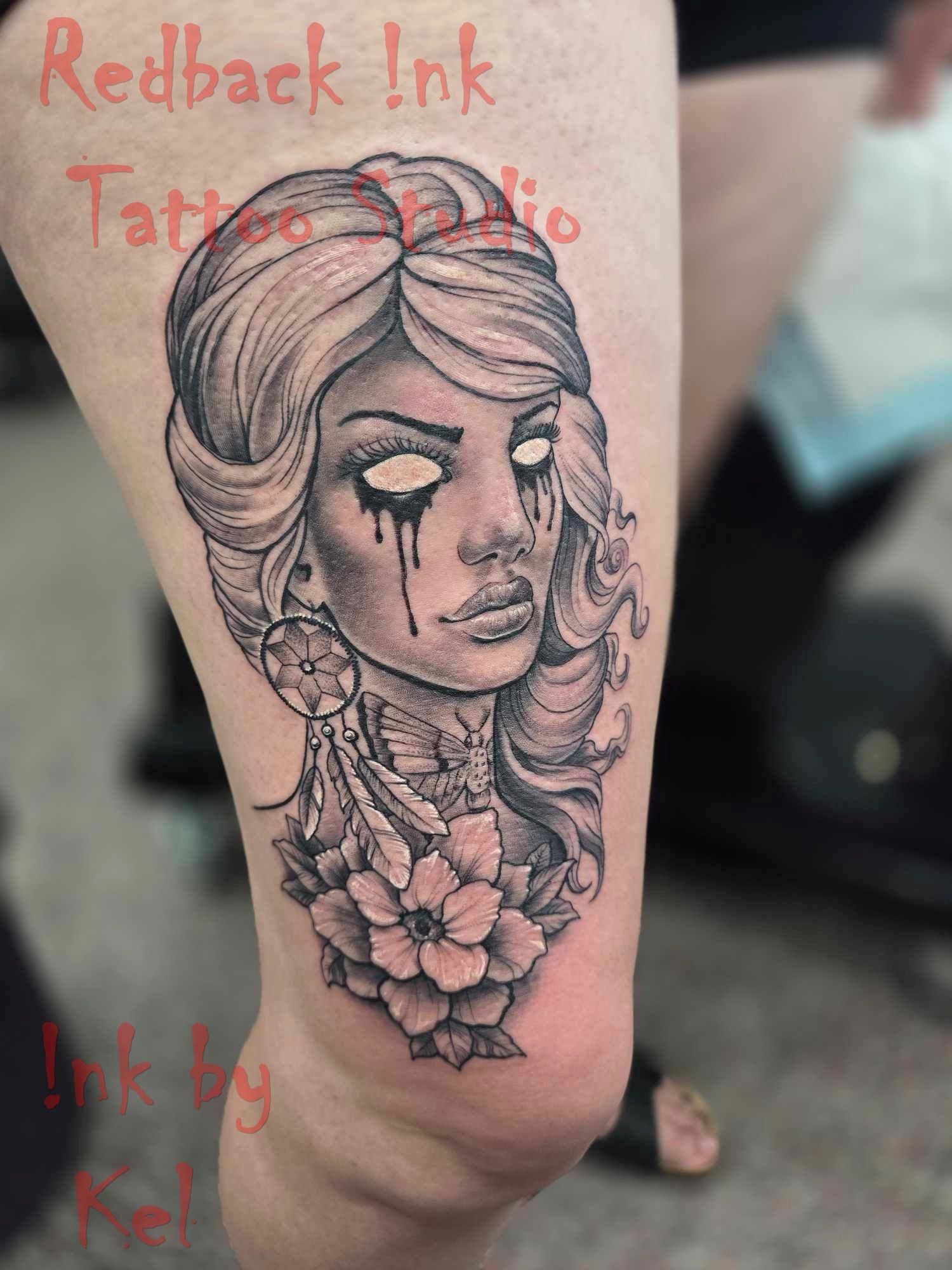 Black and gray tattoo of a woman with empty eyes and a floral collar on a person's thigh. — Redback !nk Tattoo Studio in Kawana, QLD