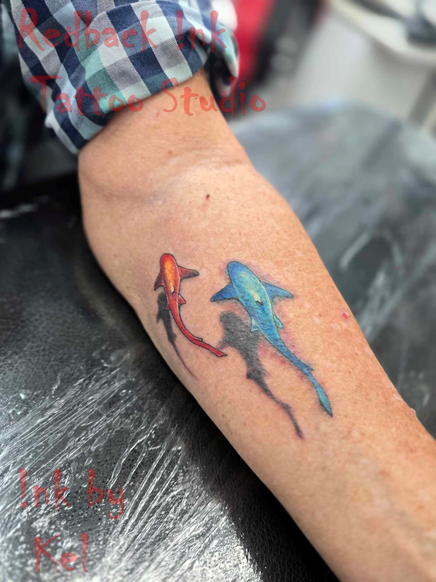 Tattoo of two colorful koi fish on a person's arm. Red and blue fish swim together, with a shadow.
