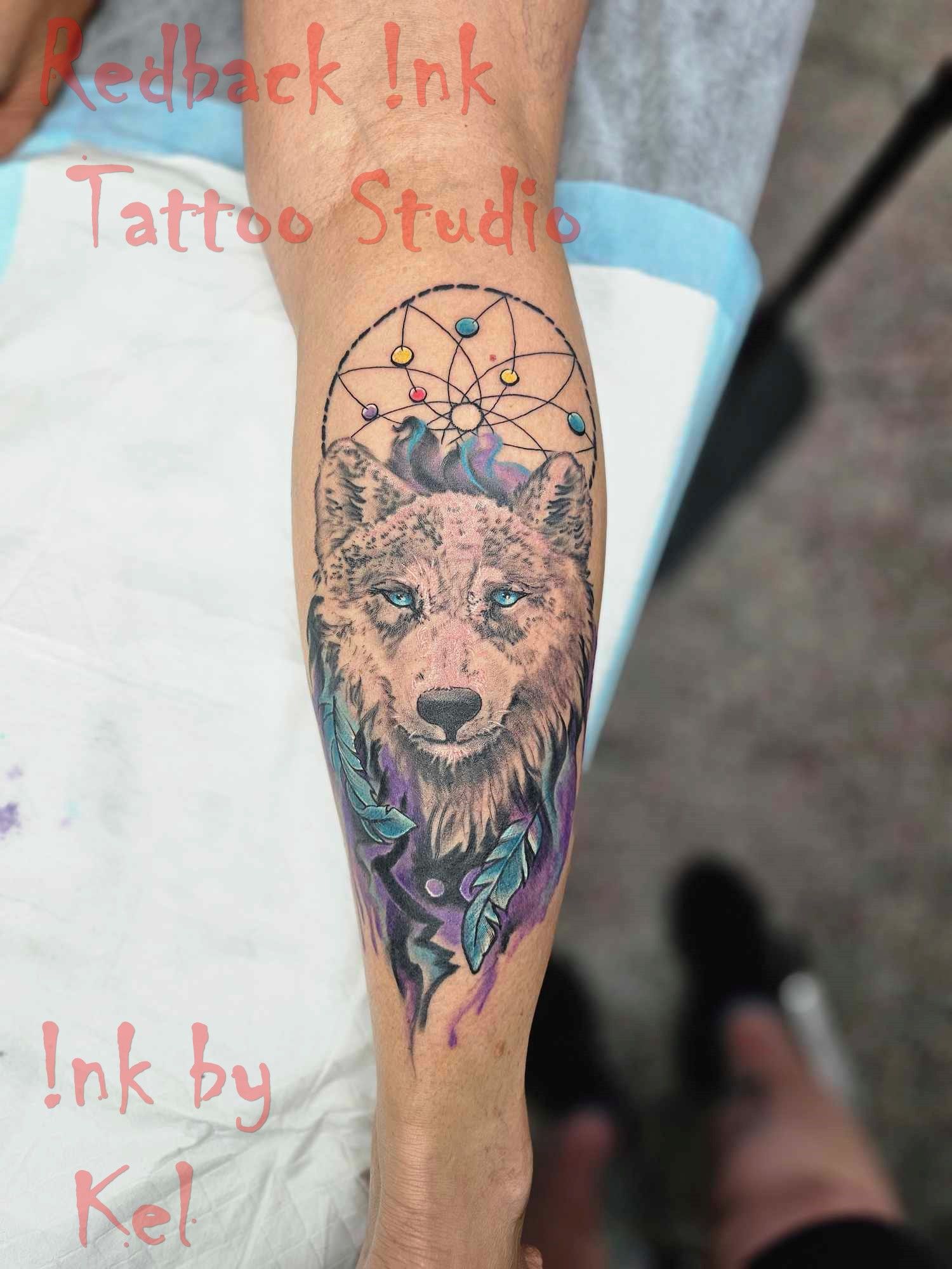 Leg tattoo: wolf head, dreamcatcher, colorful feathers. 