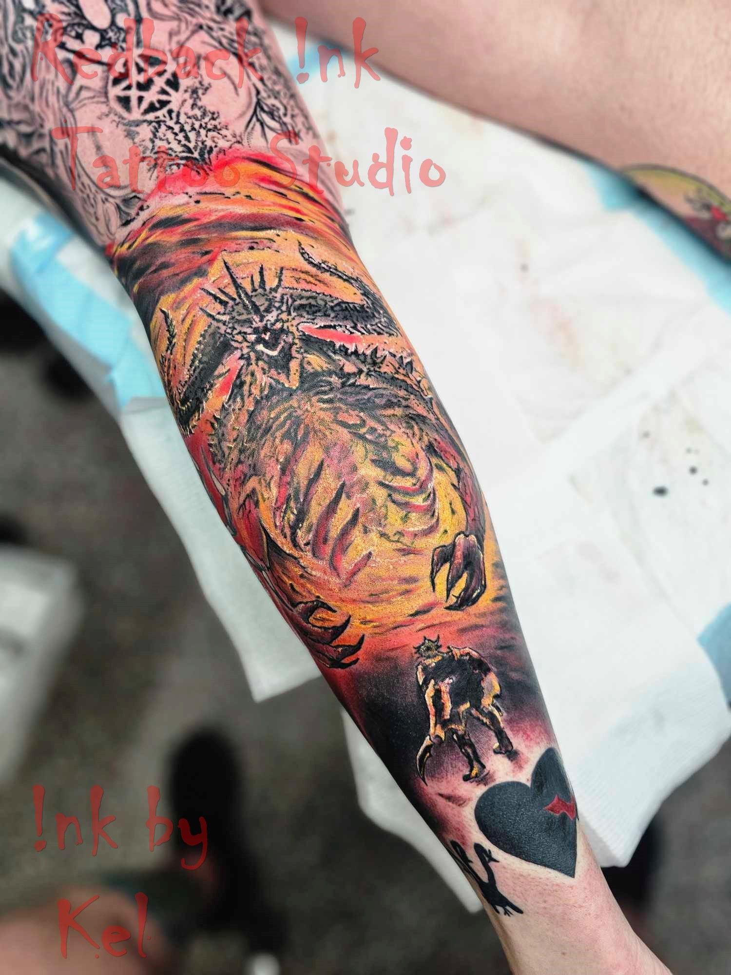 Tattoo of a hellscape scene on an arm. Includes a fiery sky, skeletal figures, and a playing card heart.