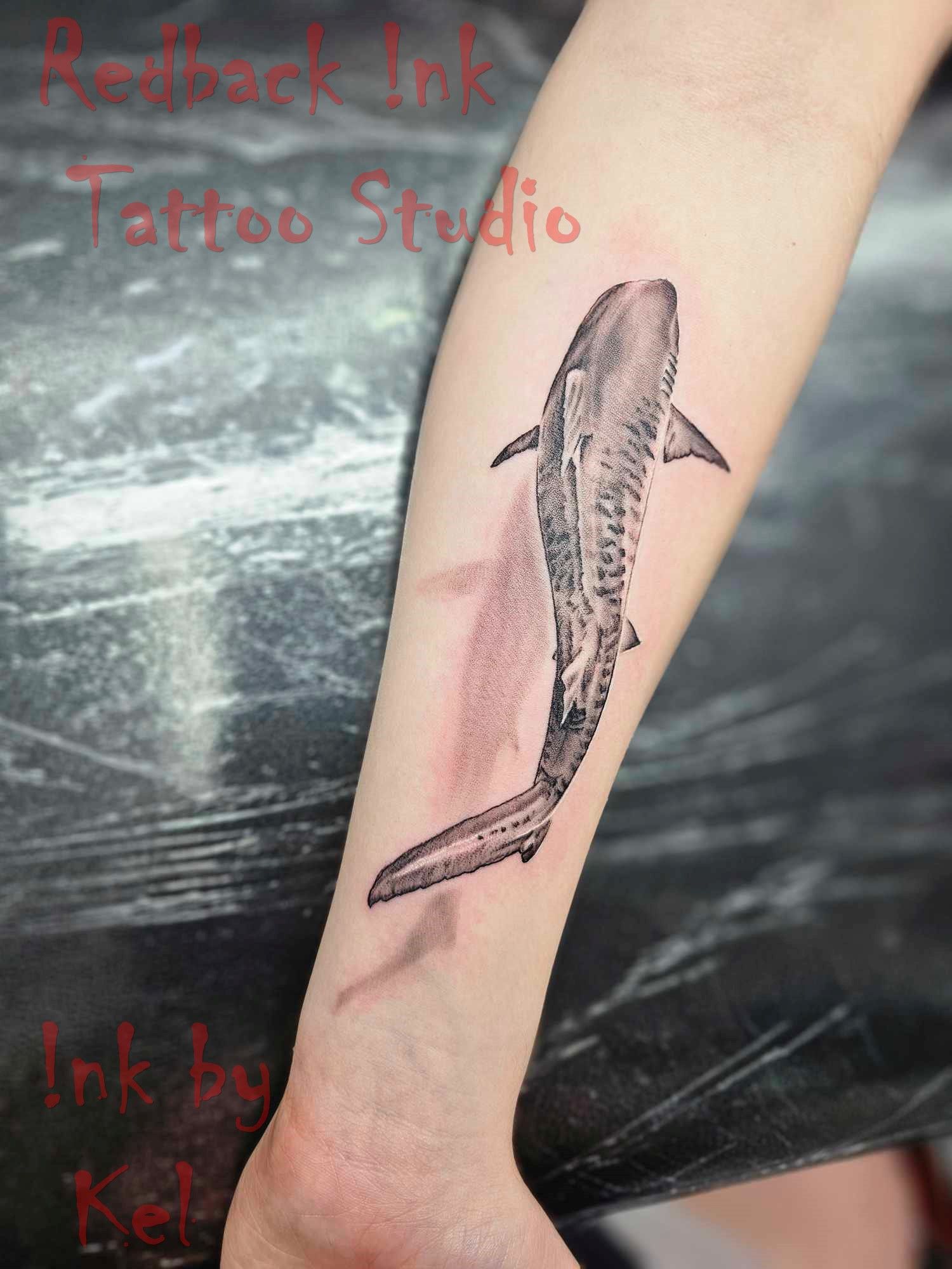 Shark tattoo on a person's forearm in black and white with a shadow.