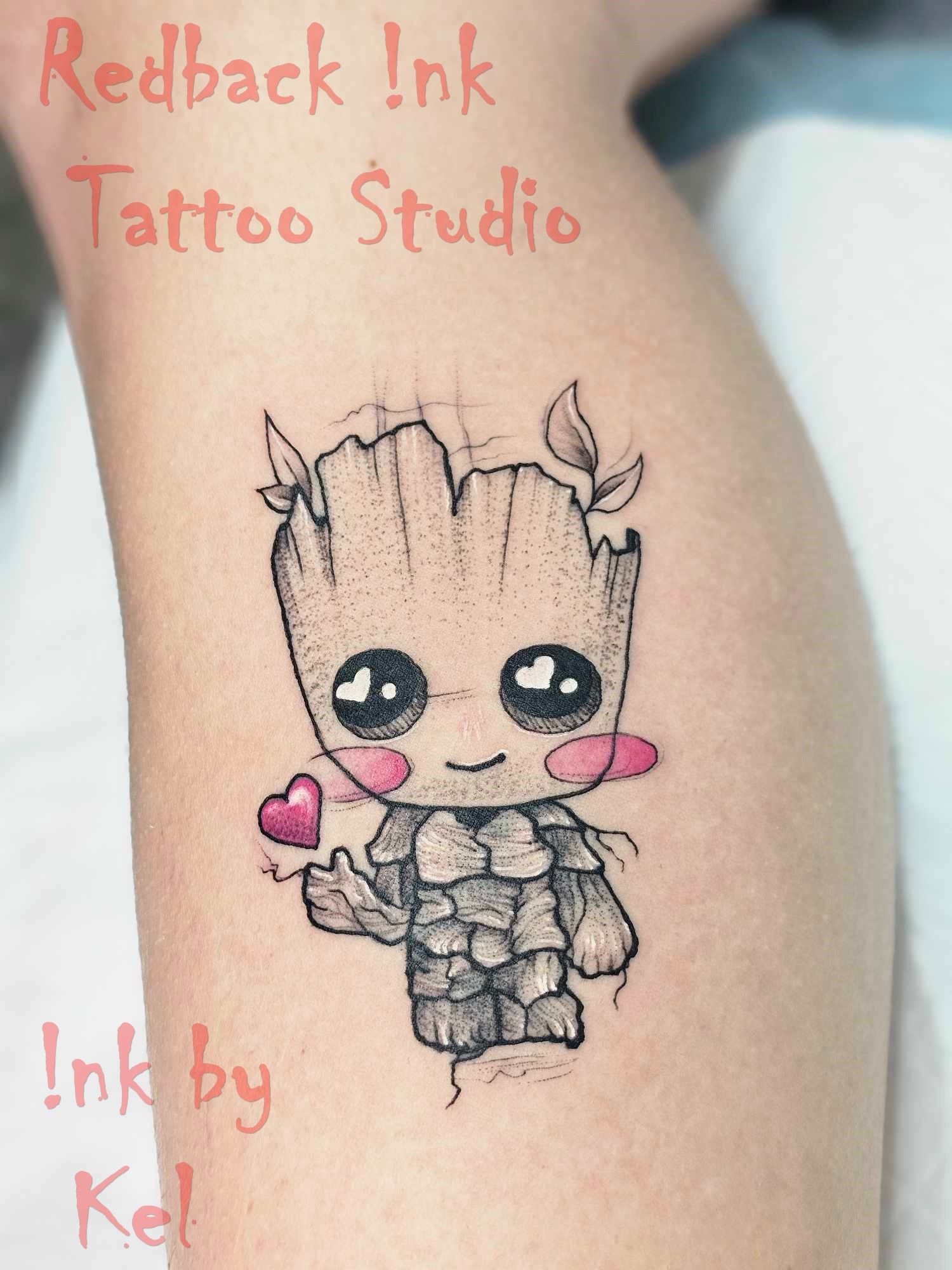 Cute Baby Groot tattoo with heart, blush, and leaves. Located on arm, with studio name and artist.