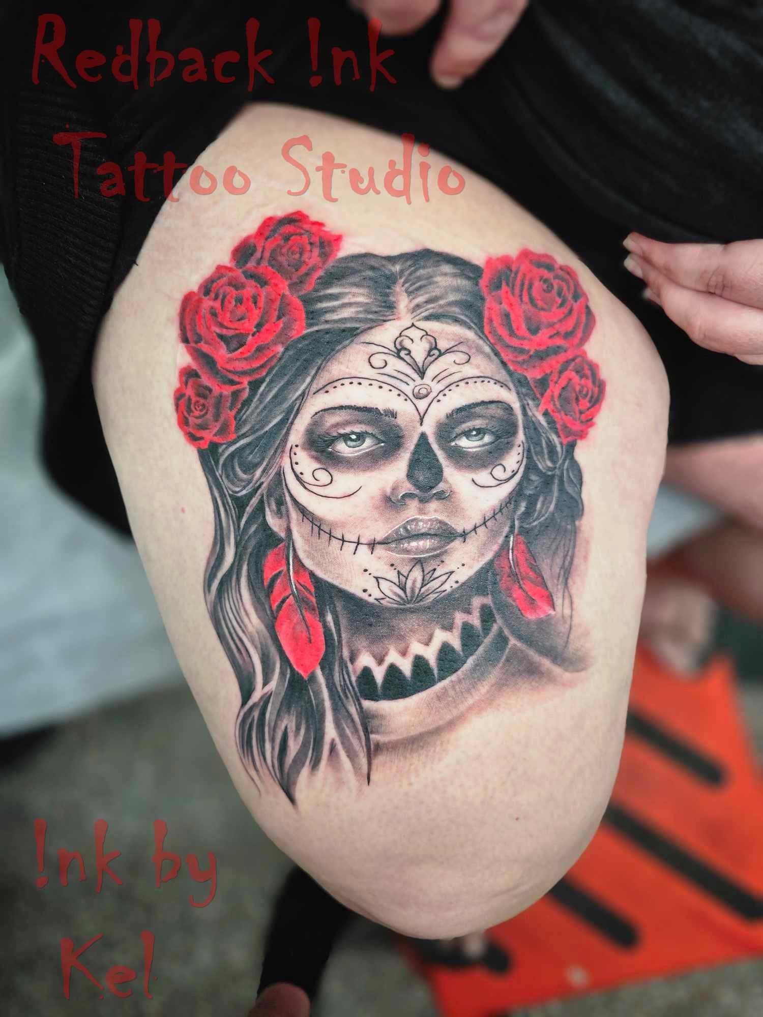 Sugar skull tattoo with red roses, on a thigh. Black and gray with red accents.