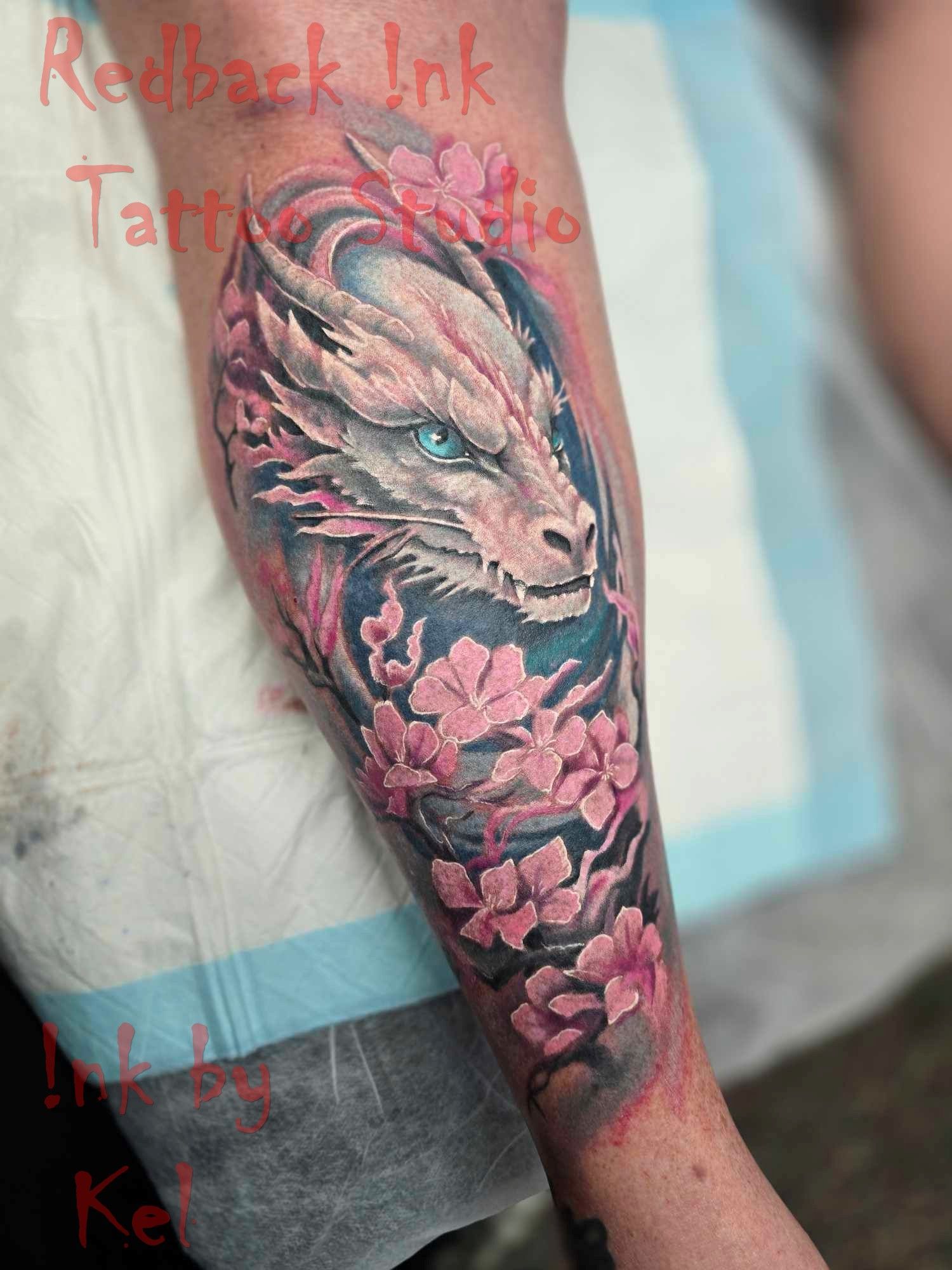 Tattoo of a white dragon head with blue eyes and pink cherry blossoms on a forearm. — Redback !nk Tattoo Studio in Kawana, QLD