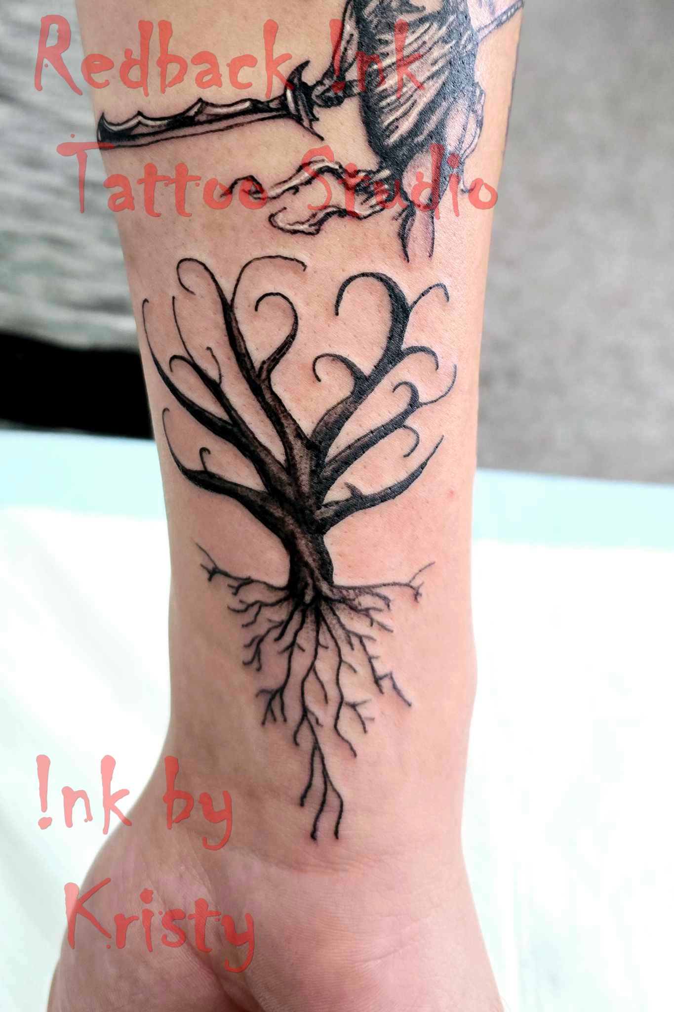 Black tree tattoo with detailed roots and curly branches on a wrist — Redback !nk Tattoo Studio in Kawana, QLD
