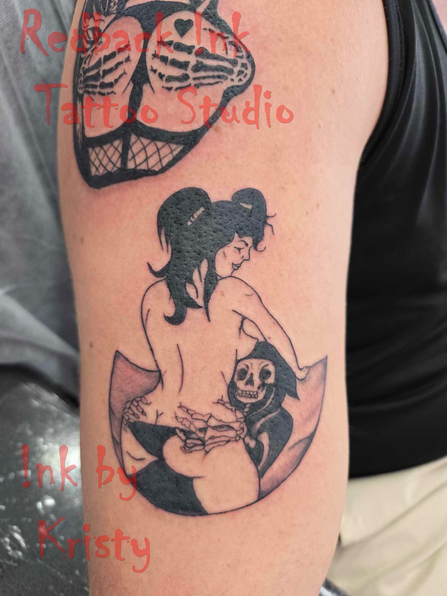 Tattoos: Woman riding a skeleton; heart-shaped skeleton buttocks above. Black ink on arm — Redback !nk Tattoo Studio in Kawana, QLD