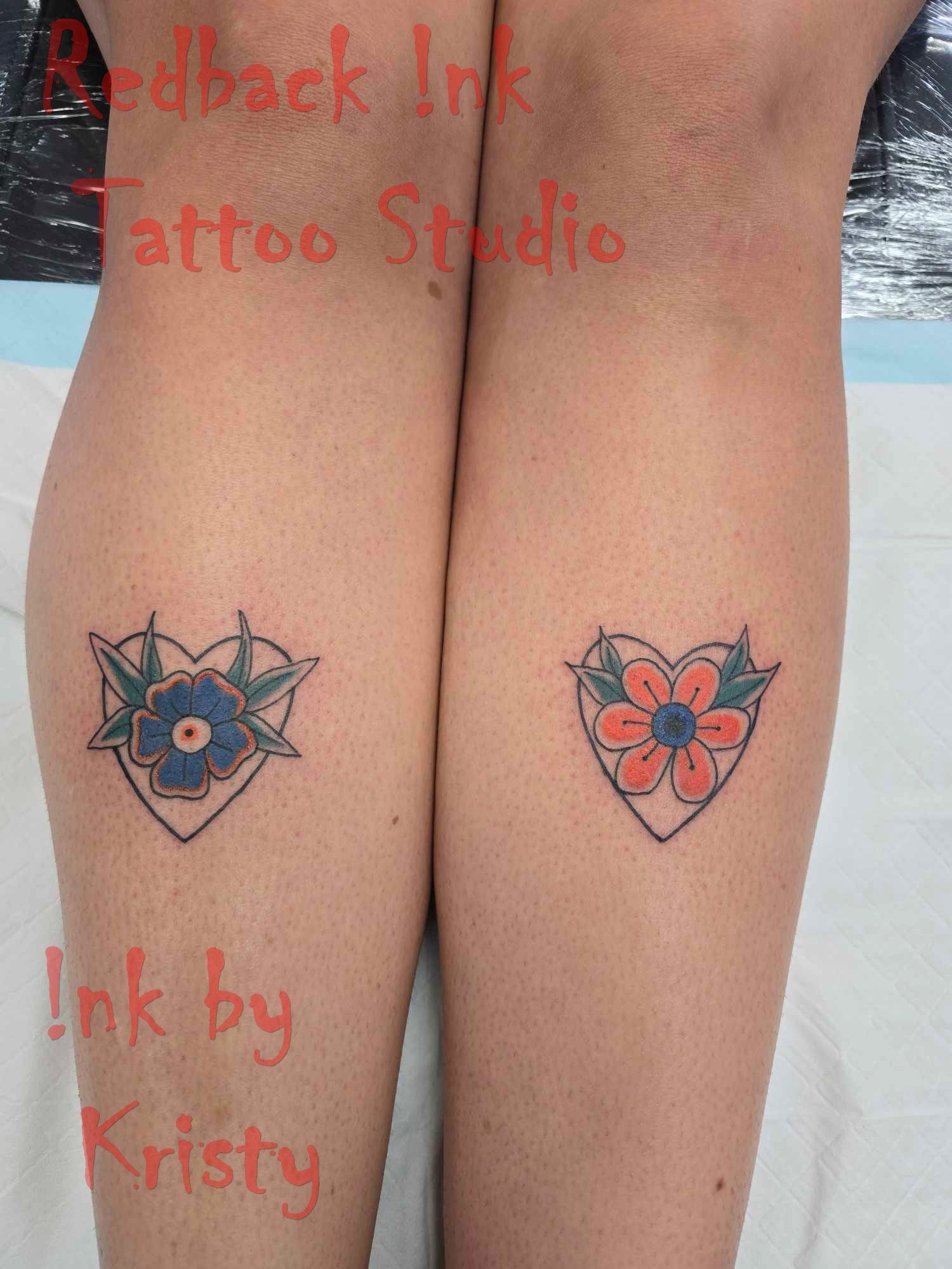 Two leg tattoos of heart-shaped flowers, one blue and one orange, on the lower legs — Redback !nk Tattoo Studio in Kawana, QLD