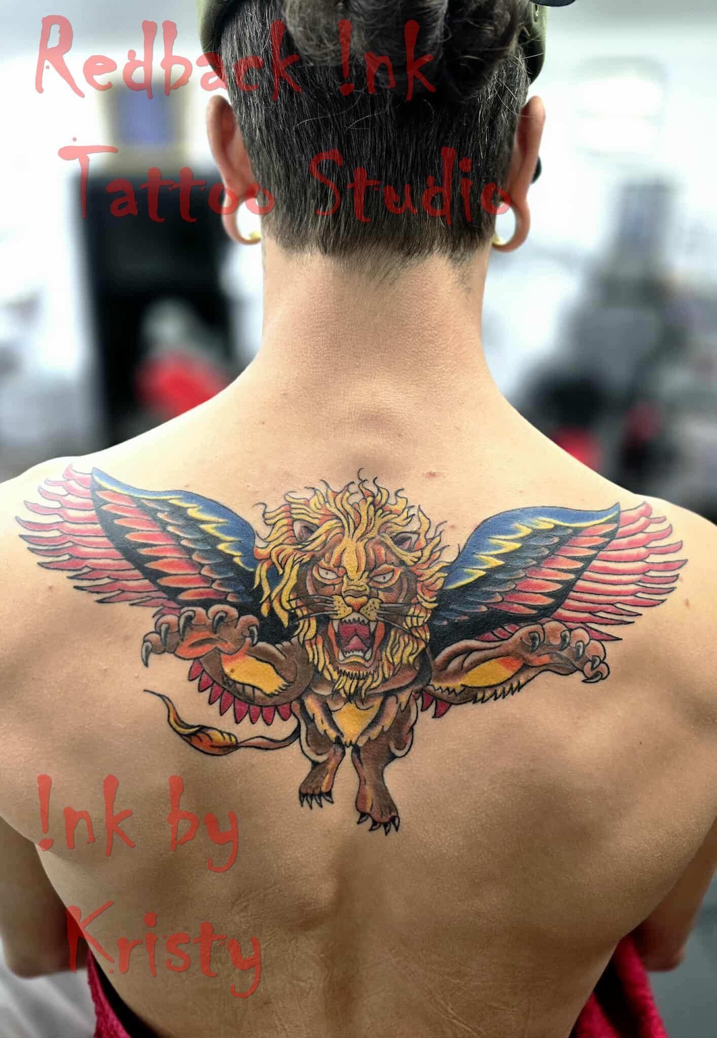 Back tattoo of a winged lion, with red, yellow, and black details. A person with dreadlocks is showing it off — Redback !nk Tattoo Studio in Kawana, QLD
