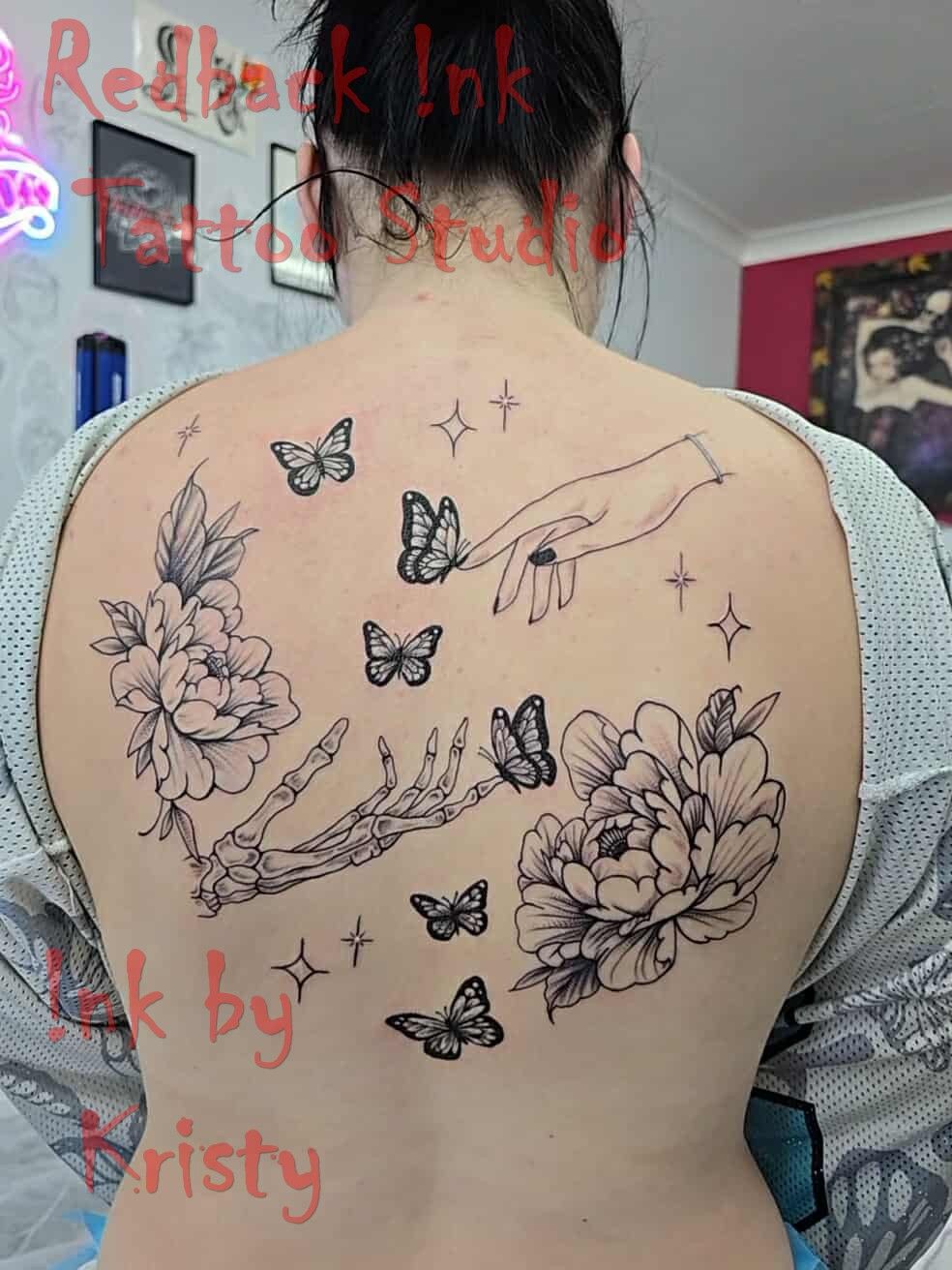 Back tattoo: Flowers, butterflies, skeletal hand, reaching hand, stars. Black ink — Redback !nk Tattoo Studio in Kawana, QLD
