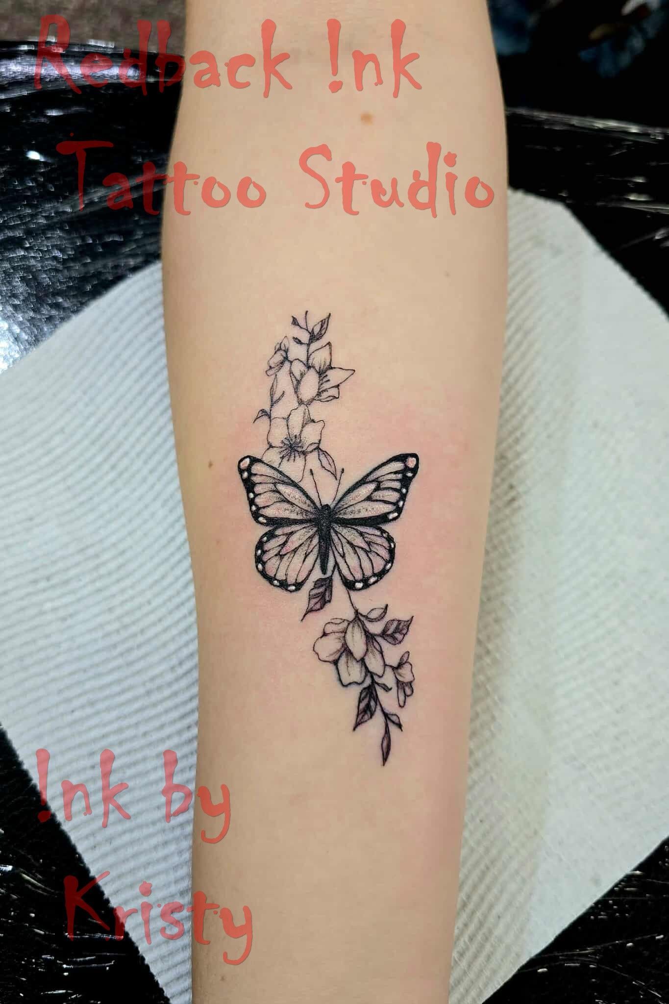 Black butterfly tattoo on forearm with floral accents, by Kristy at Black Ink Tattoo Studio — Redback !nk Tattoo Studio in Kawana, QLD