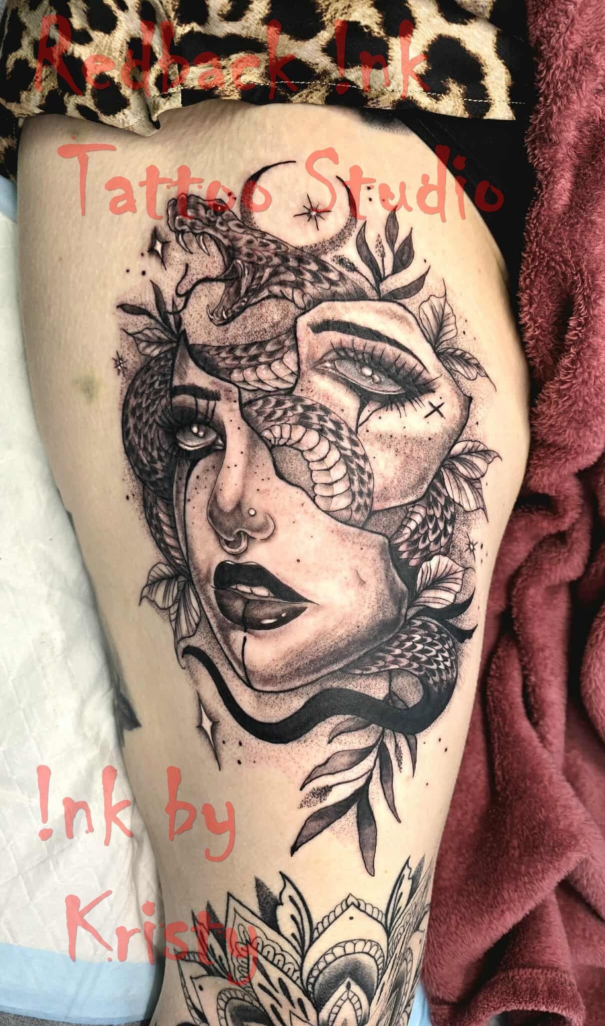 Tattoo of a woman's face with snake and floral elements on a thigh. Black and white ink — Redback !nk Tattoo Studio in Kawana, QLD