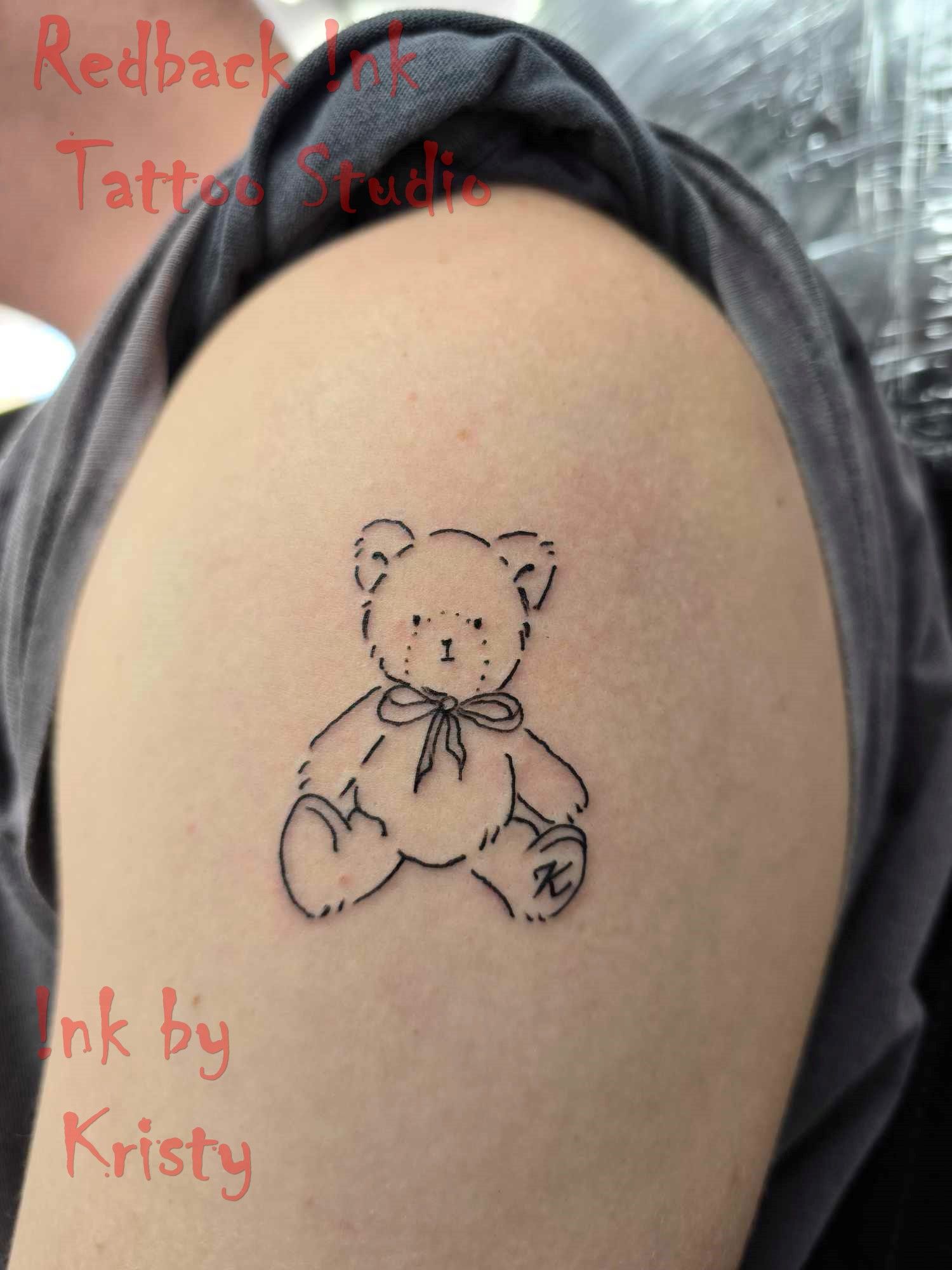 A black outline tattoo of a teddy bear on a person's upper arm — Redback !nk Tattoo Studio in Kawana, QLD