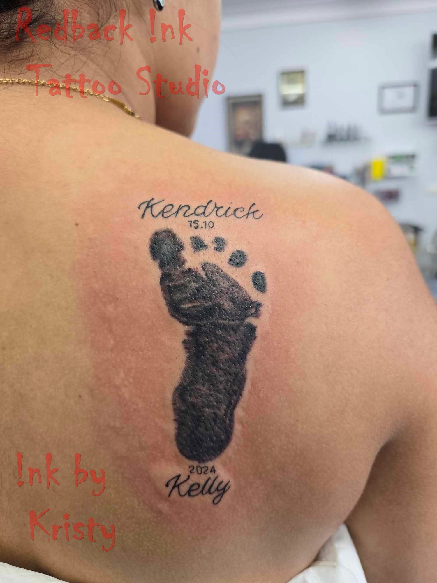 Tattoo of a baby footprint on a person's back, with the baby's name and date, along with the mother's name — Redback !nk Tattoo Studio in Kawana, QLD