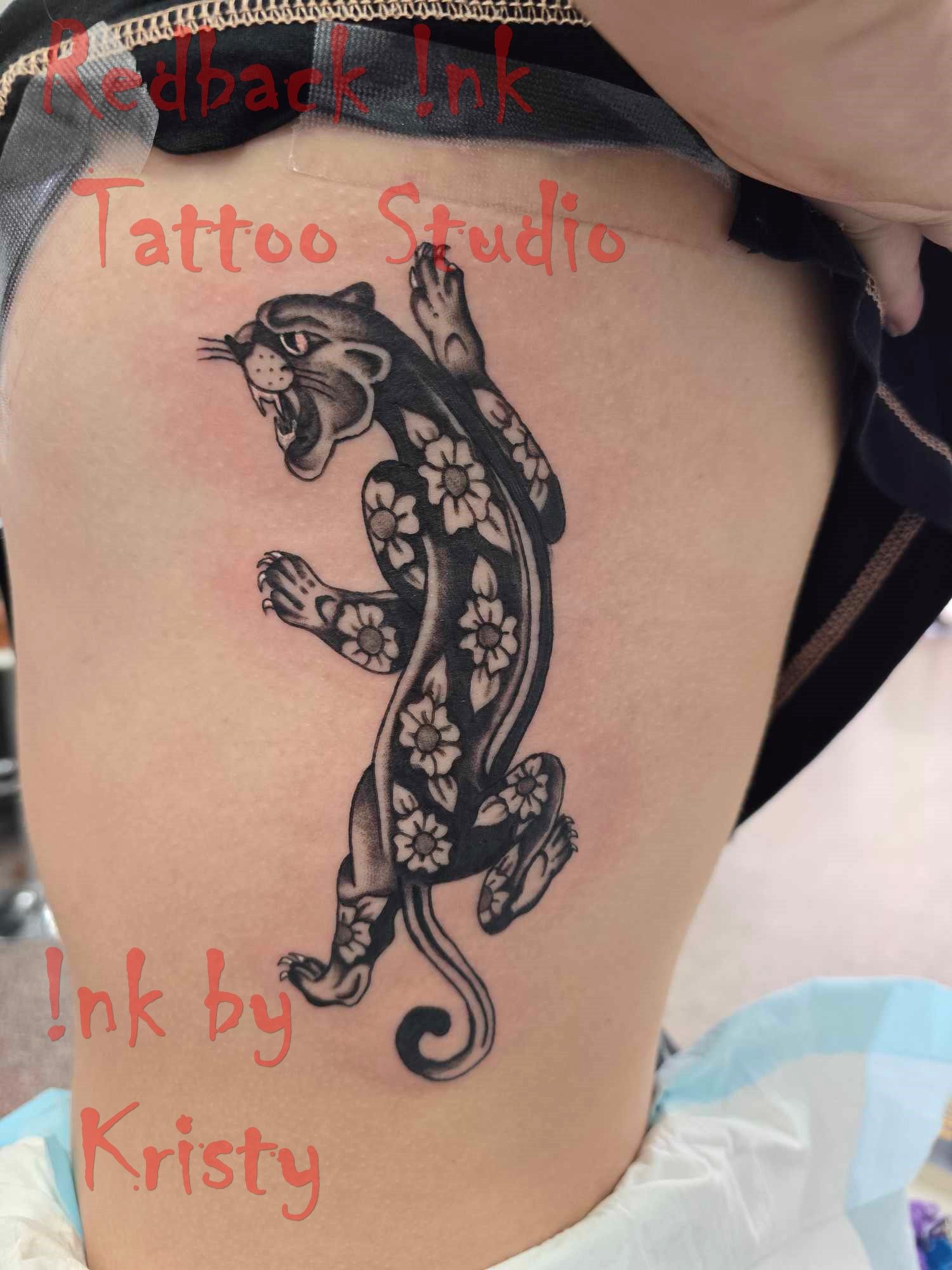 Black panther tattoo with floral details on a person's side. 