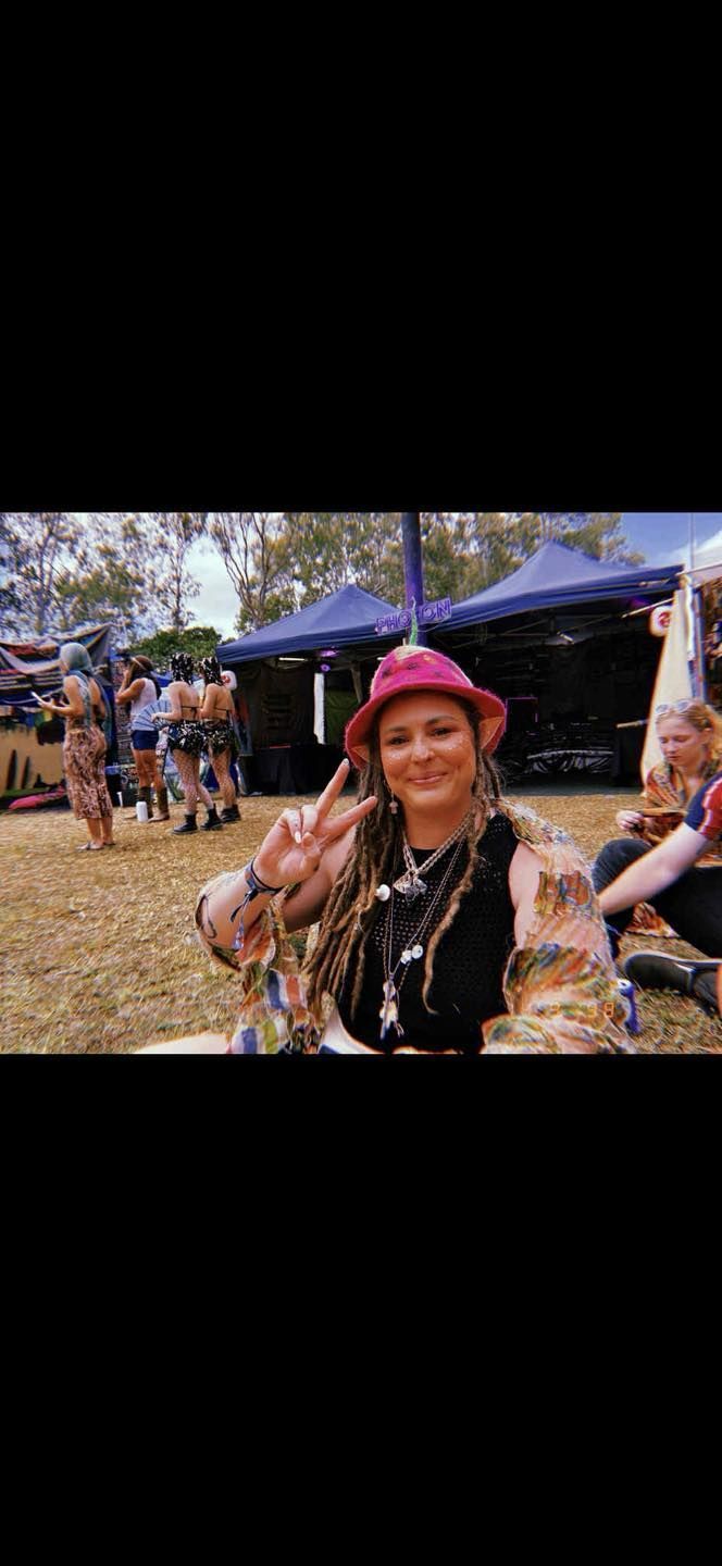 Smiling person in a pink hat at an outdoor market, with stalls and people in the background.
