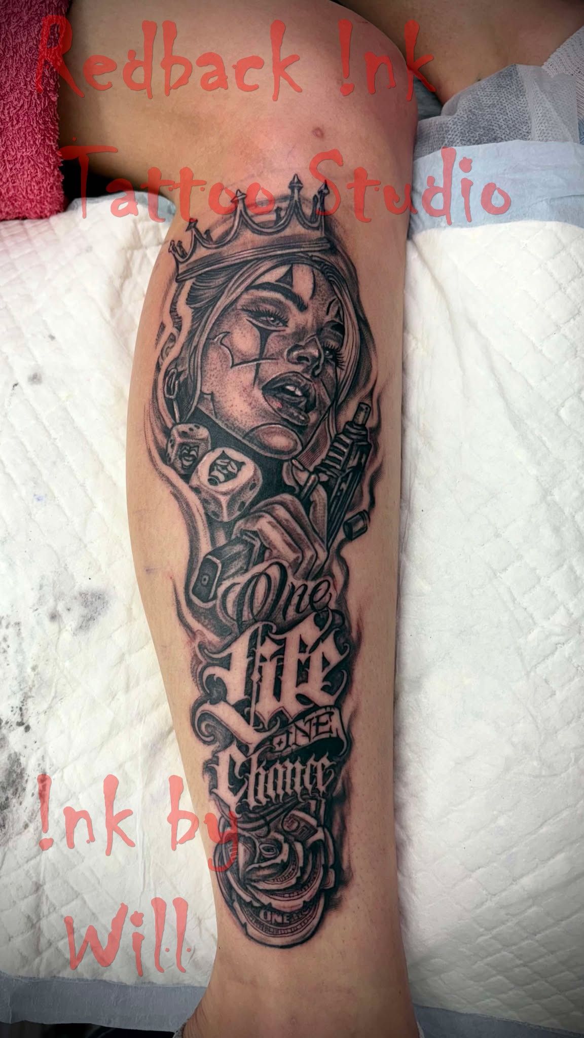 Leg tattoo of a clown face wearing a crown, surrounded by scrollwork and text 