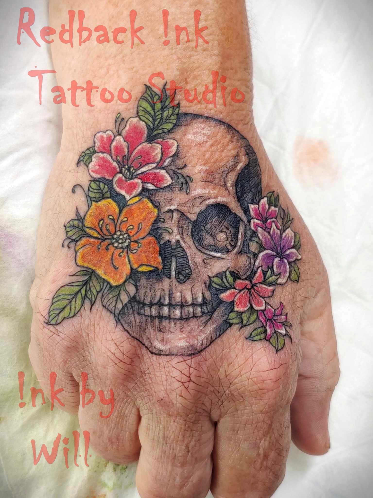 Skull tattoo with colorful flowers on a hand.